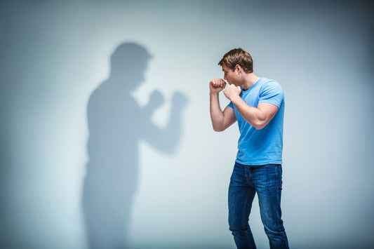 a man in boxing stance with guard up looking at his own shadow on the wall