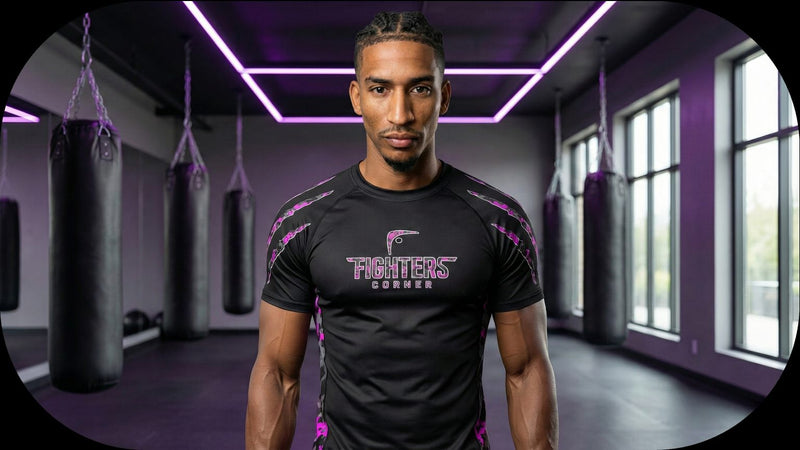 Fighters Corner founder Jeremy Emebe wearing a branded black and pink camo performance rash guard standing in a modern boxing gym with heavy bags.